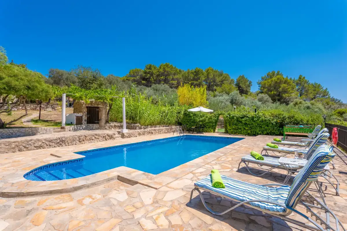 An outdoor swimming pool sits beside a paved patio with lounge seating.