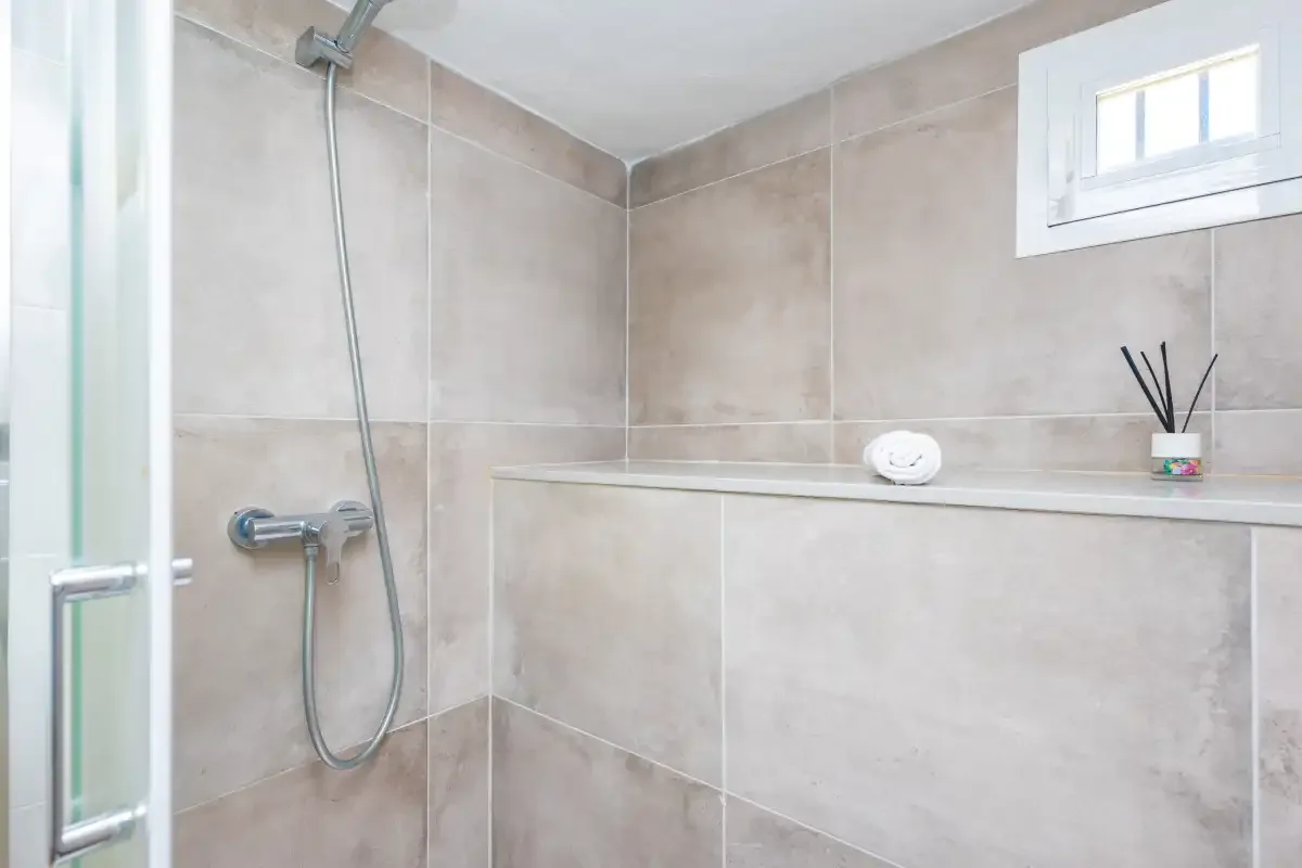 A tiled bathroom shower with a small window and toiletries on a ledge.