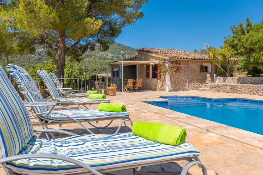 A swimming pool beside a stone-paved patio with striped loungers and greenery.