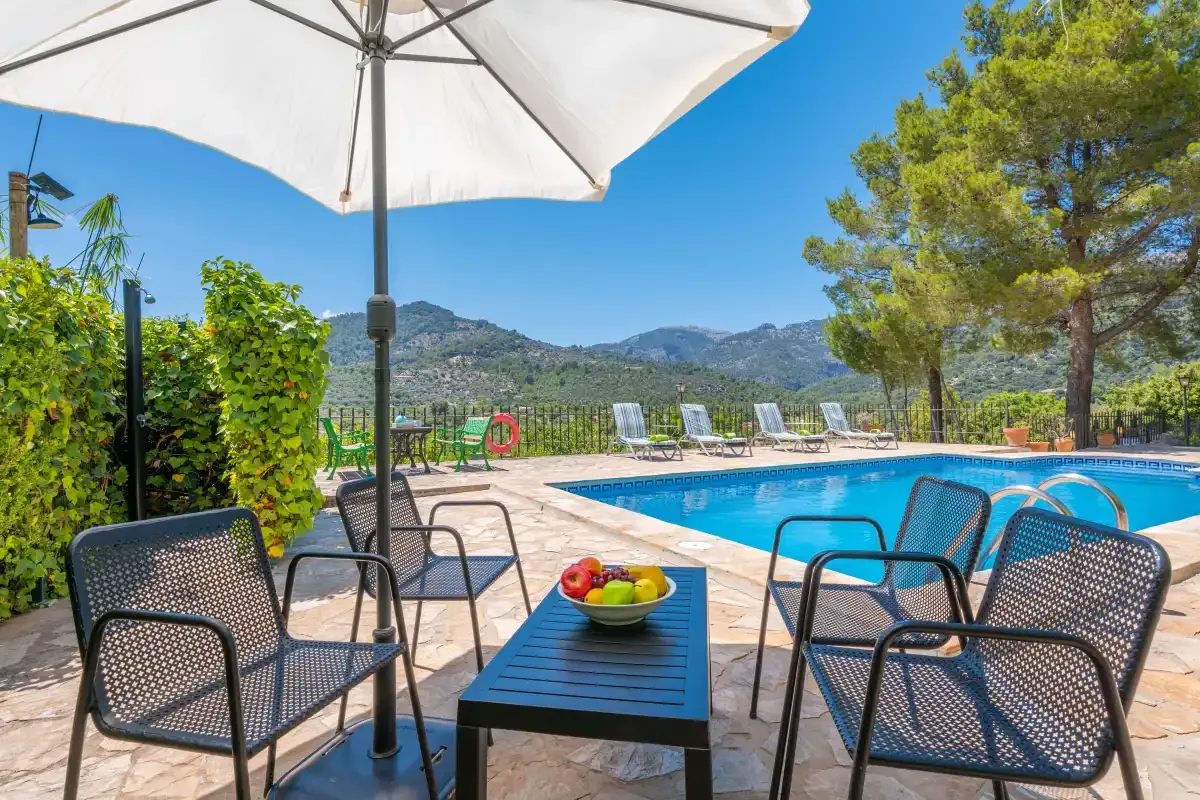 An outdoor pool area with seating, an umbrella, and mountain views.