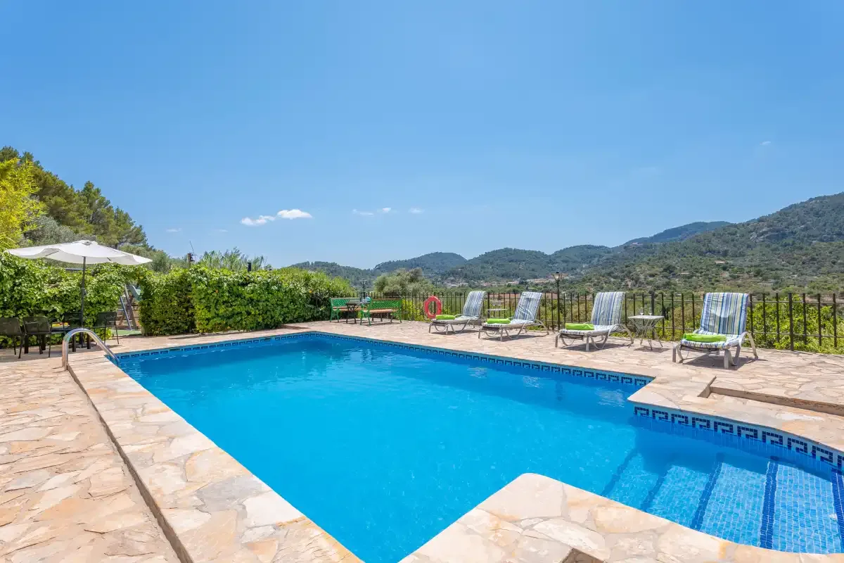 An outdoor swimming pool sits beside a stone patio with hills in the background.