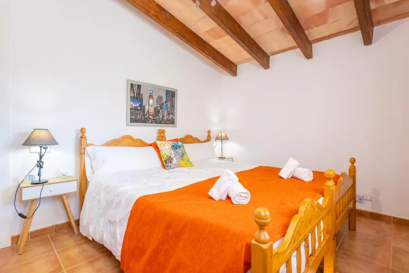 A bedroom with a wooden bed covered in white and orange bedding.