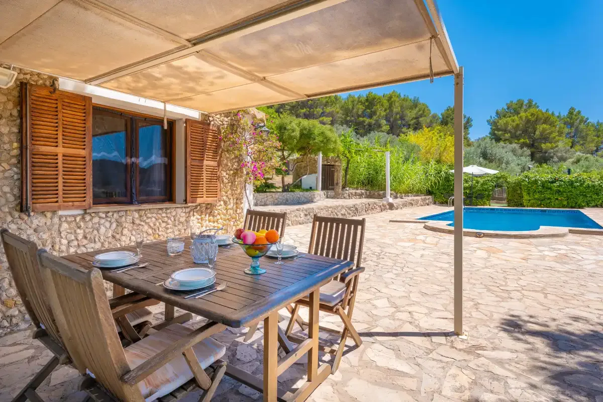 A shaded outdoor dining area overlooks a swimming pool and garden.