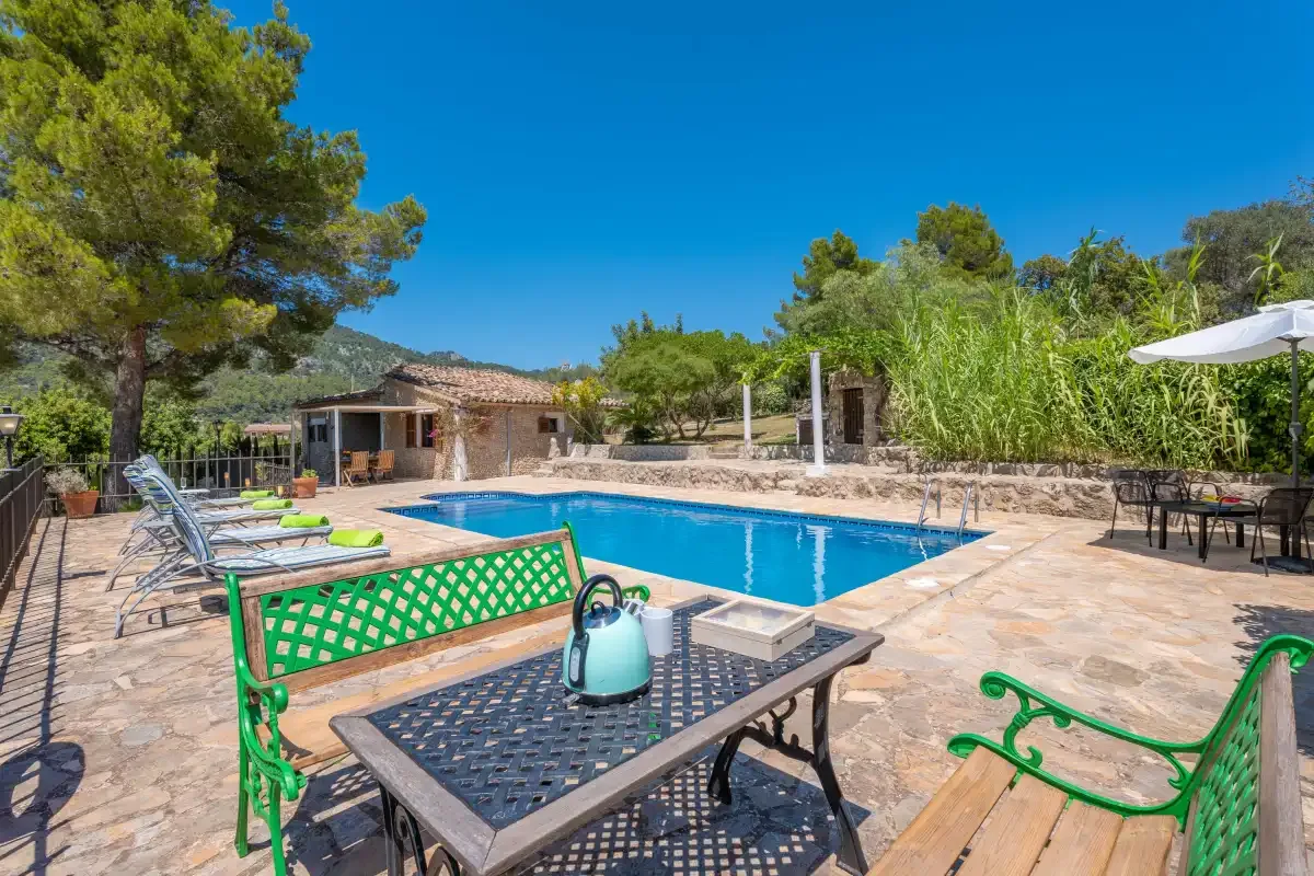 An outdoor swimming pool sits beside a stone-paved patio with seating.