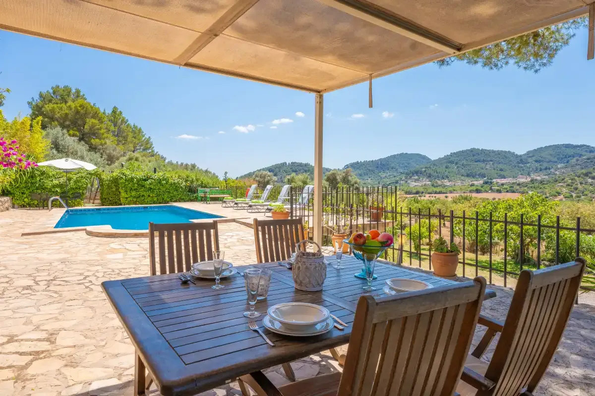 A shaded outdoor dining area overlooks a swimming pool and green hills.
