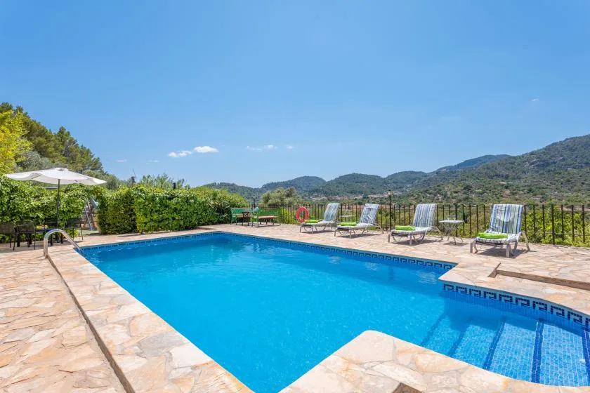 An outdoor swimming pool is surrounded by stone paving and lounge seating.