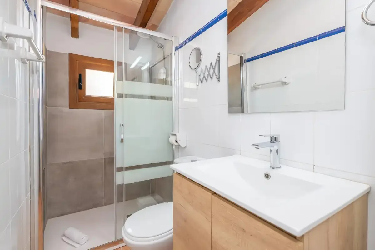 A bathroom with a shower, toilet, and sink beneath a large mirror.