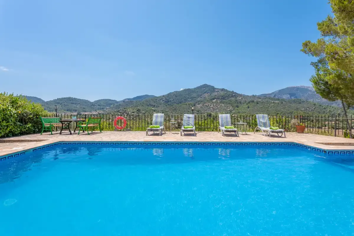 An outdoor swimming pool sits beside a terrace with loungers and mountain views.