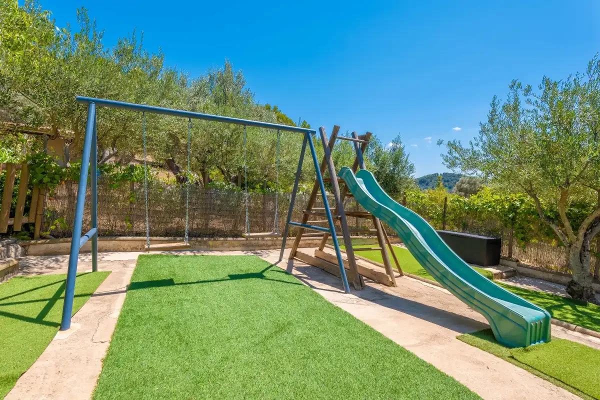 An outdoor play area with a slide and swings on green turf.