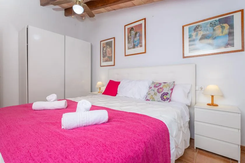 A bedroom with a bed dressed in white linens and a bright pink cover.