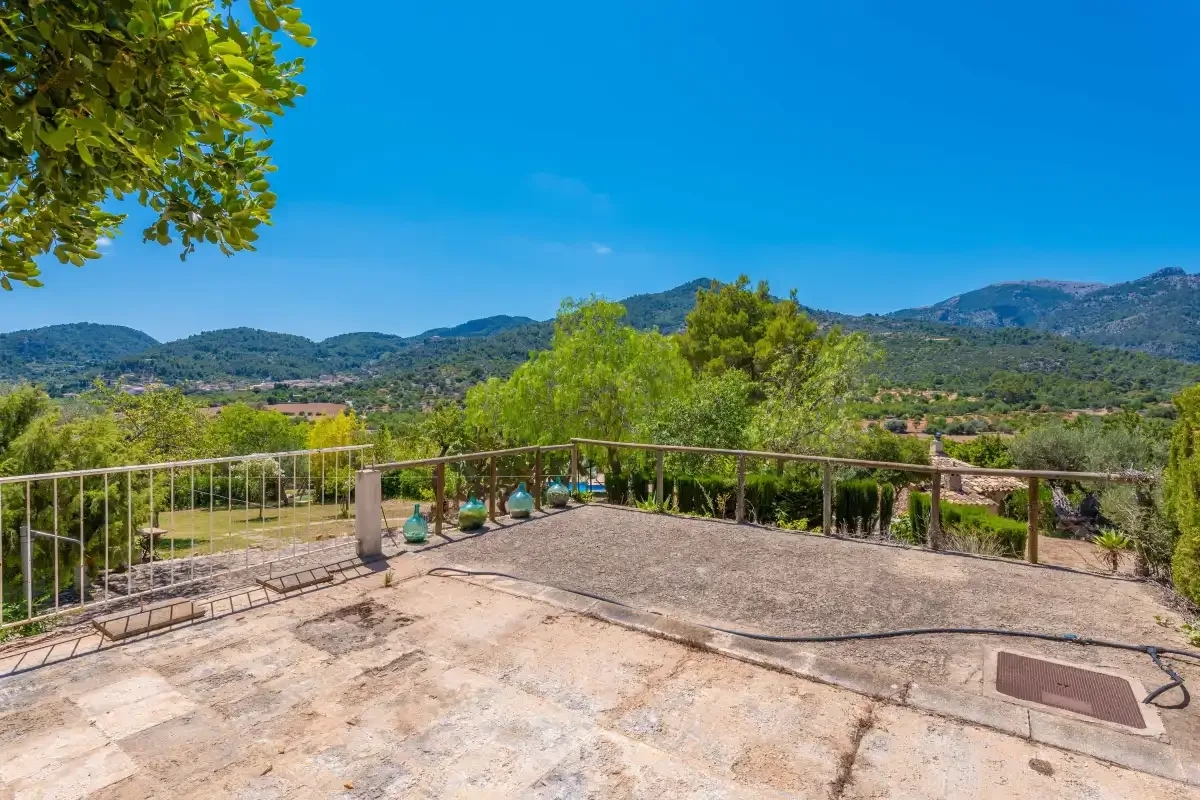A stone terrace overlooks green hills beneath a clear blue sky.