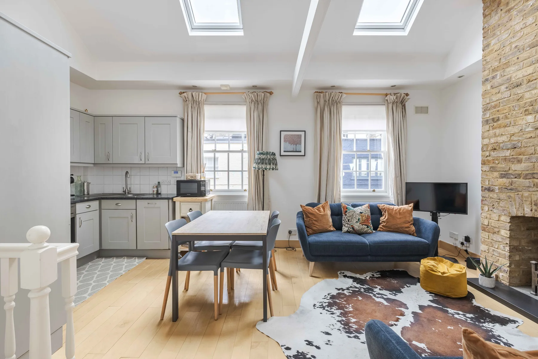 A bright living and dining area with a kitchen, blue seating, and large windows.