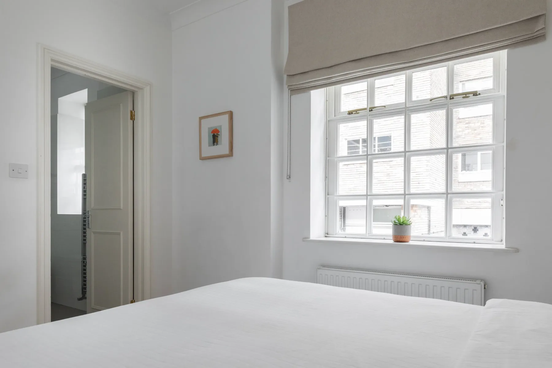 A bright bedroom with a large window and a neatly made bed.