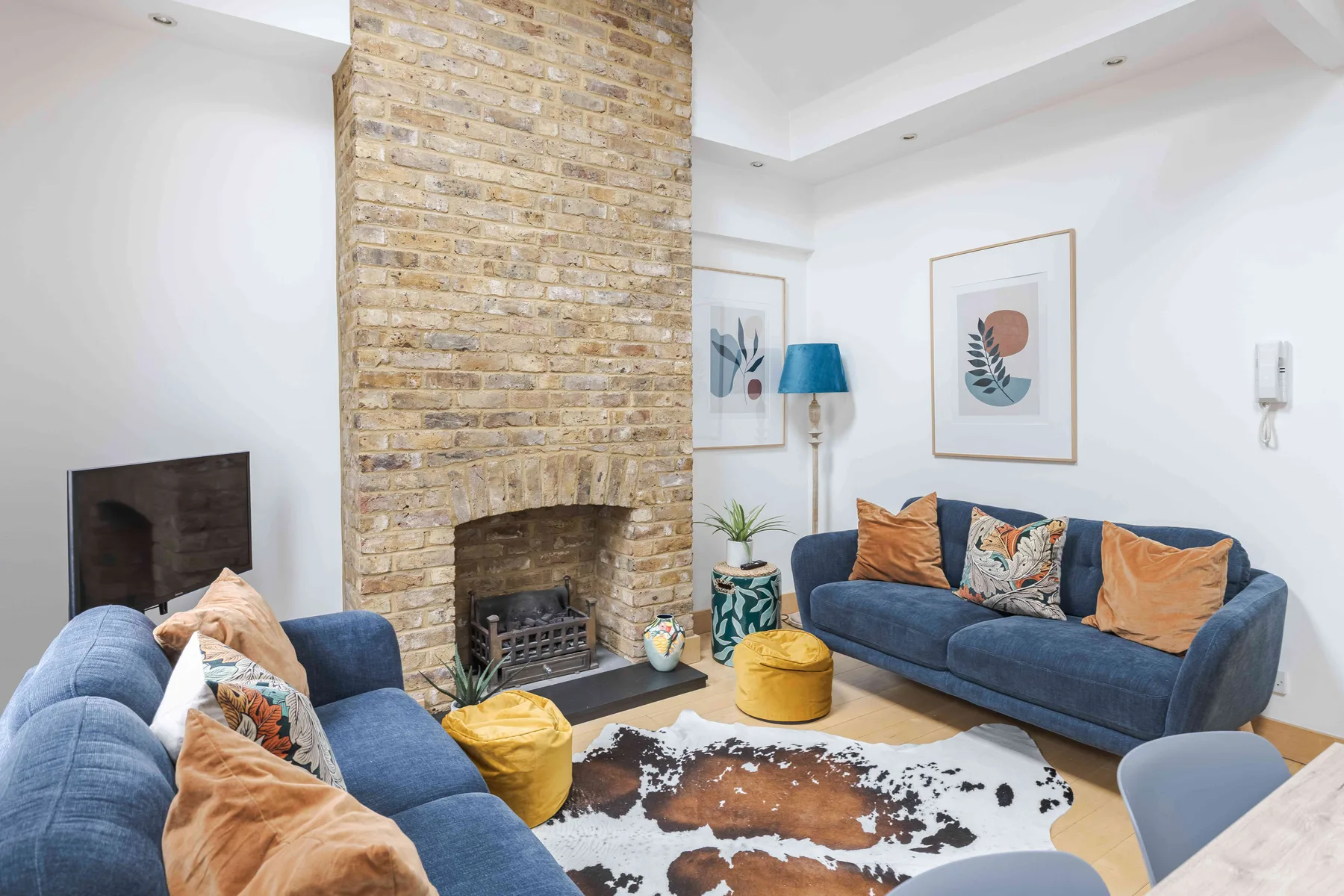 A living room with blue seating, a brick fireplace, and framed artwork.
