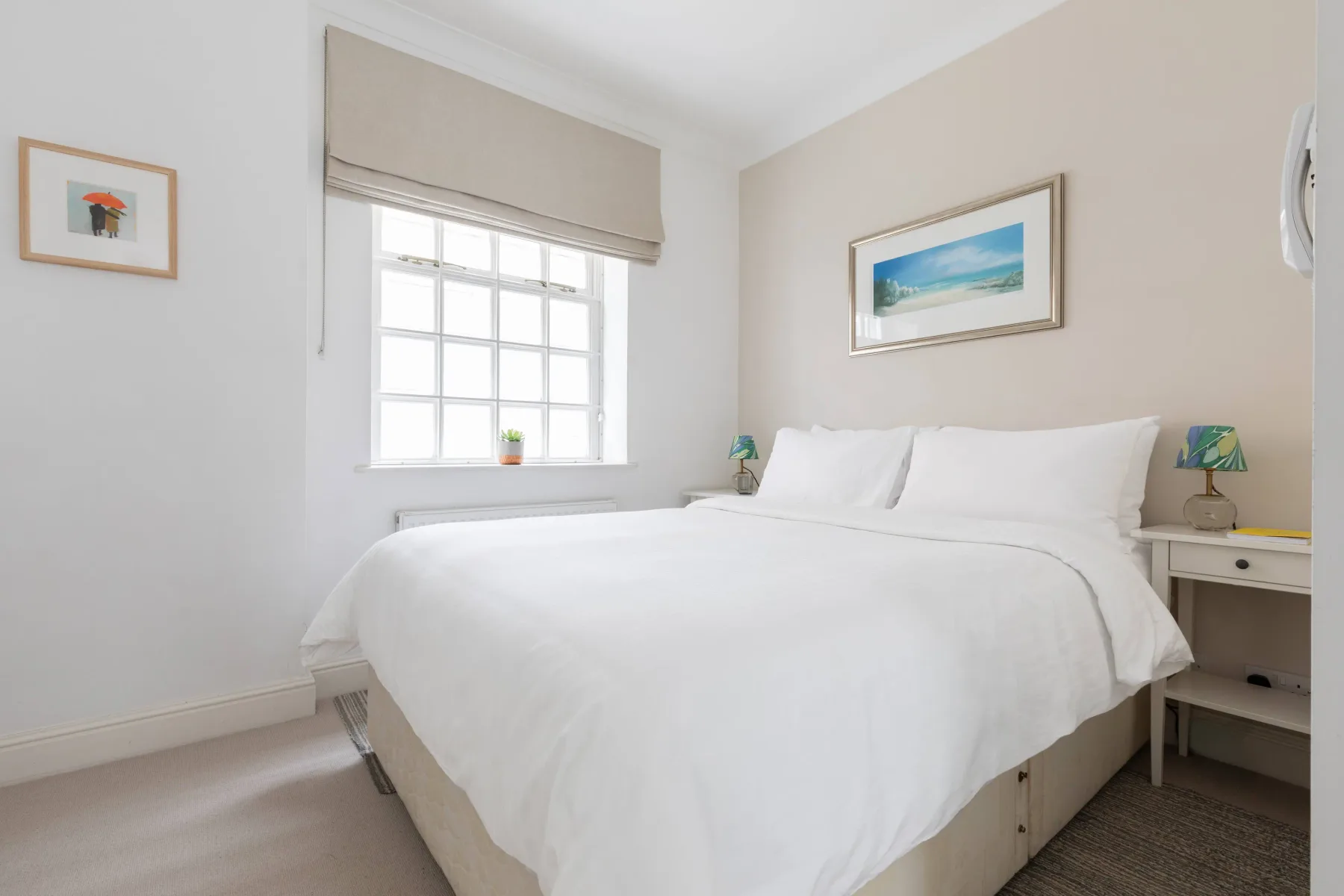 A bright bedroom with a neatly made bed and a window with a shade.