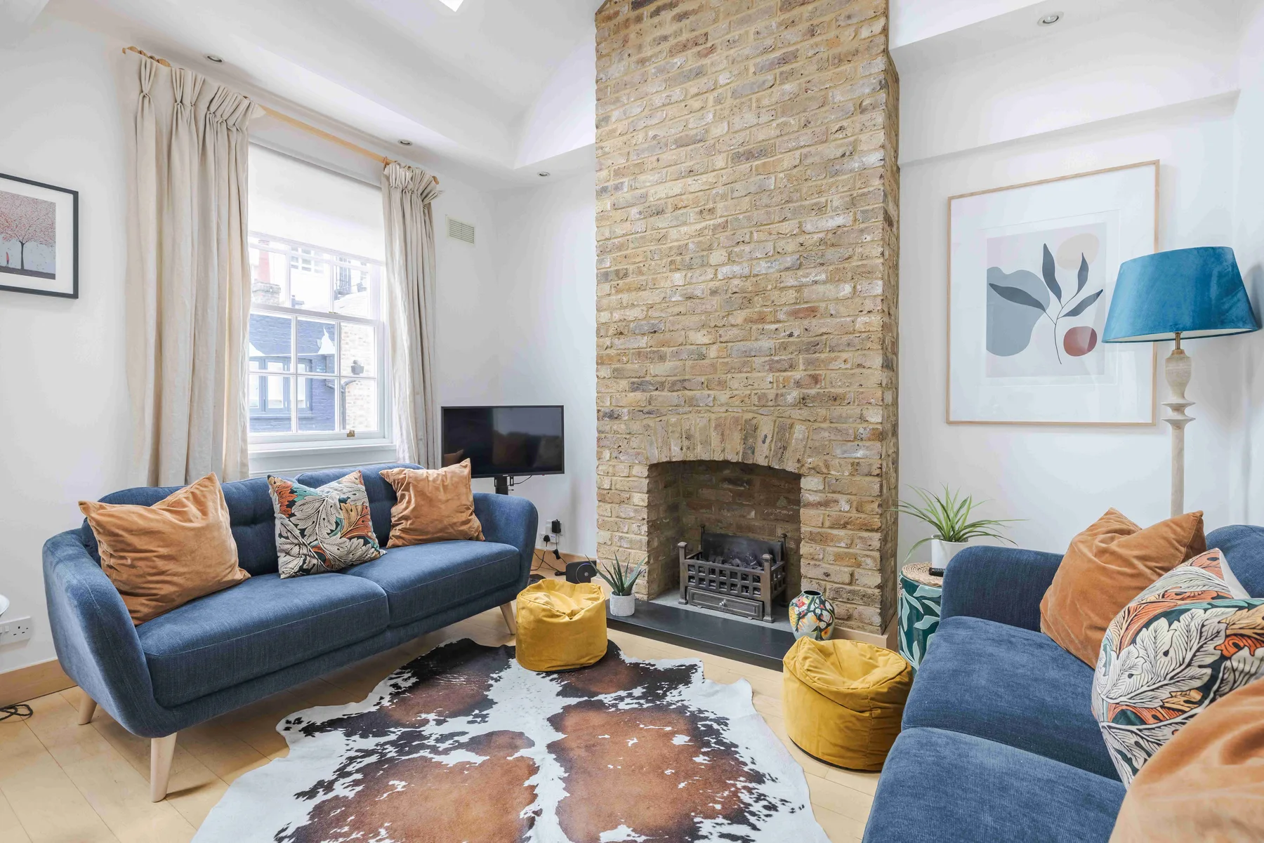 A bright living room with blue seating, a brick fireplace, and a patterned rug.