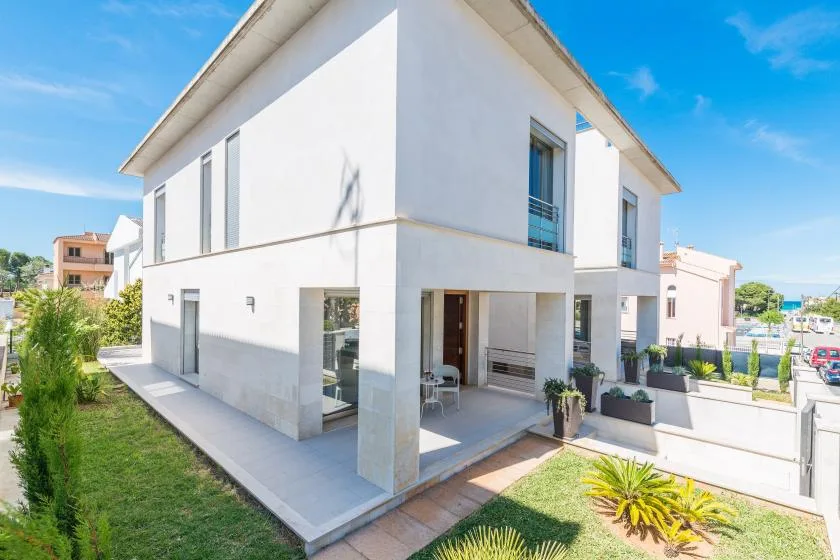 A modern white house with a covered patio and landscaped garden.
