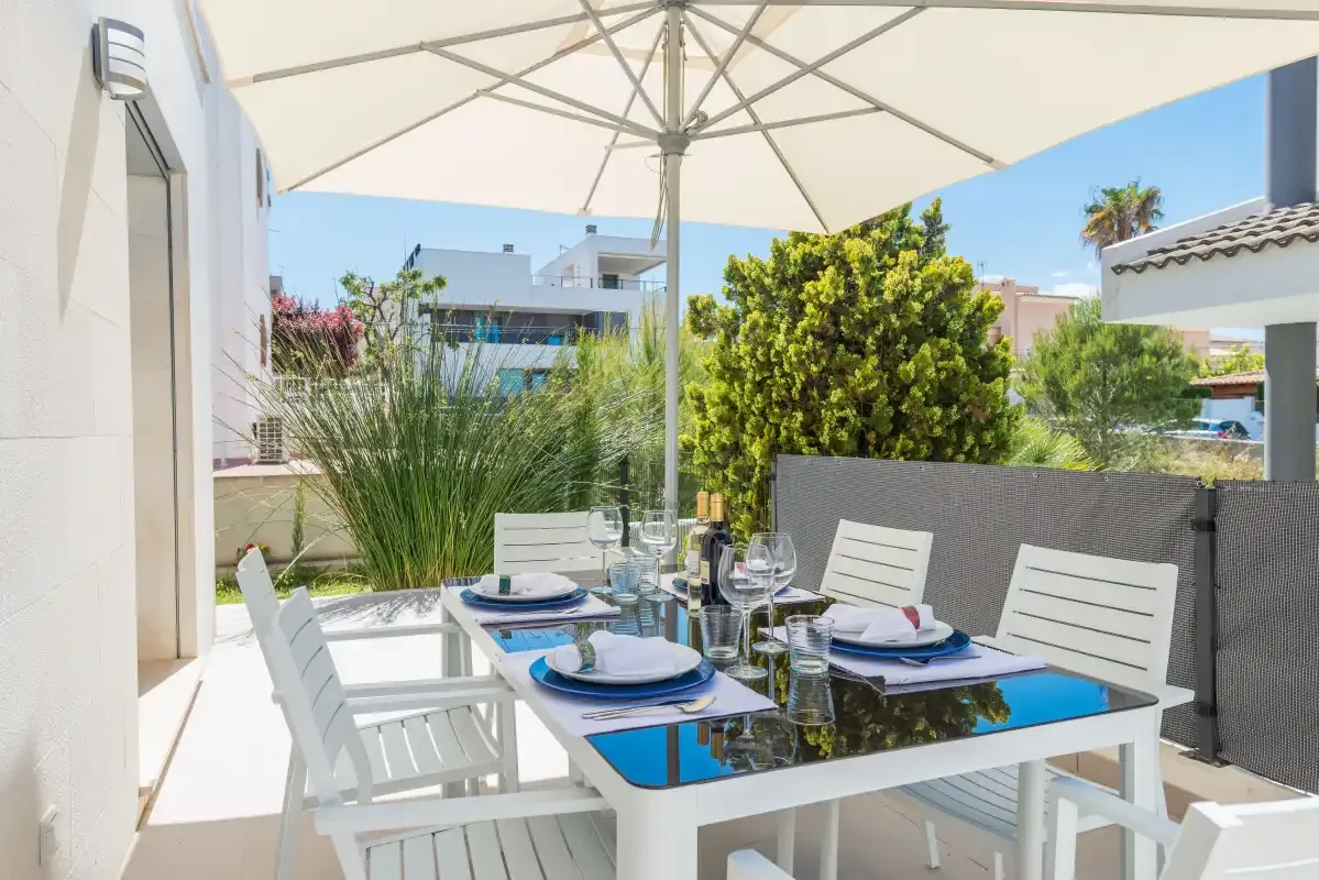 An outdoor dining table with white seating sits beneath a large patio umbrella.
