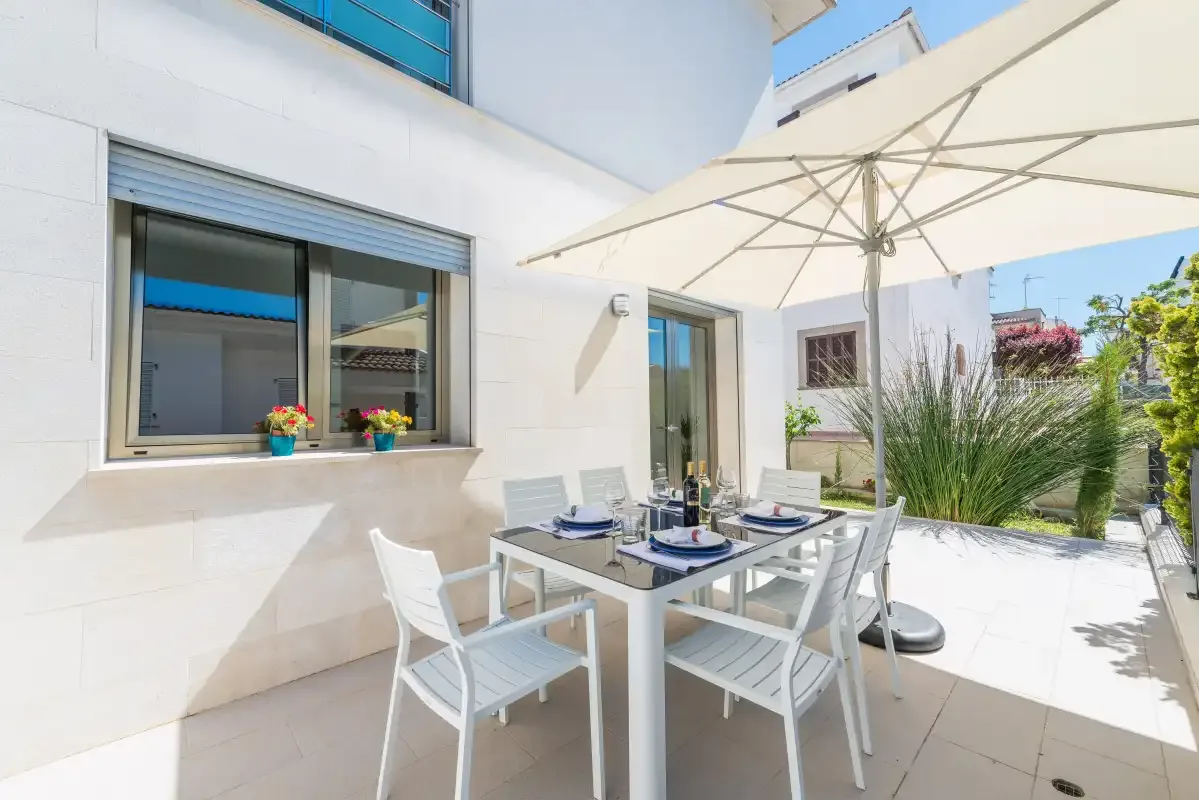 A bright outdoor dining area with a table and seating beneath a large umbrella.