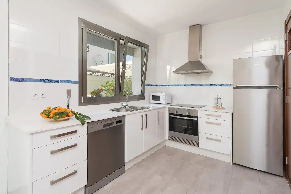 A bright kitchen with white cabinets, a window, and stainless steel appliances.