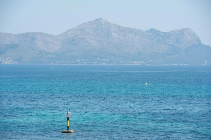 A calm expanse of blue water stretches toward a mountainous coastline.