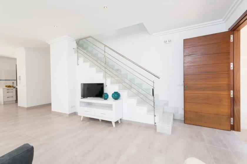 A bright living area features a staircase, television, and wooden door.