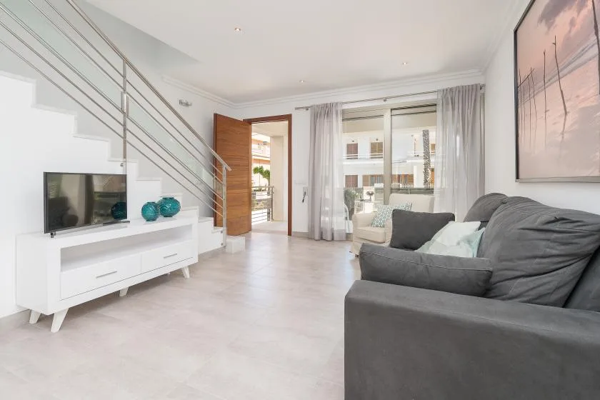 A bright living room with gray seating and a television beneath the staircase.
