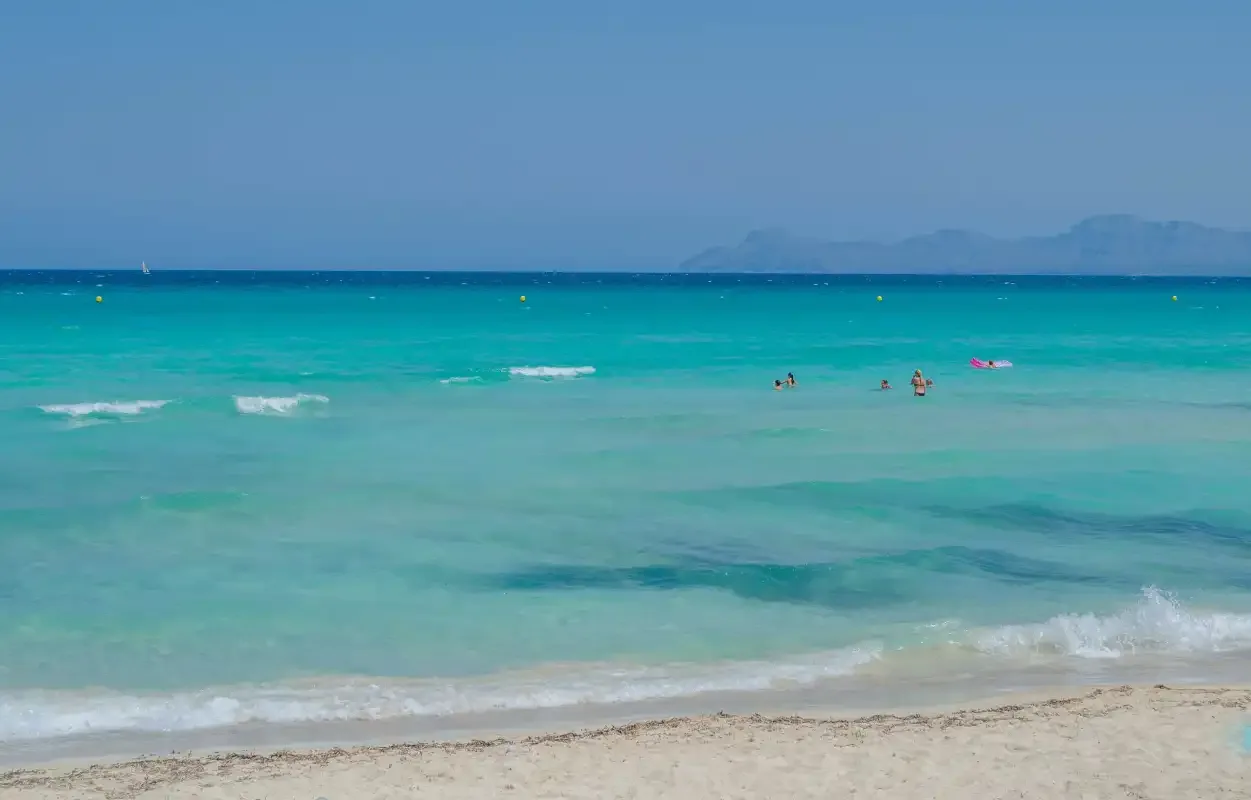 A sandy beach borders clear turquoise water beneath a blue sky.