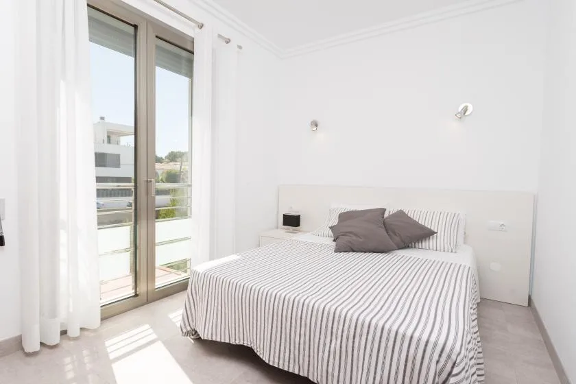 A bright bedroom with a striped bedspread beside tall glass doors.