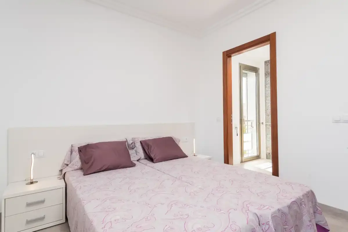 A bright bedroom with a double bed and an open doorway.