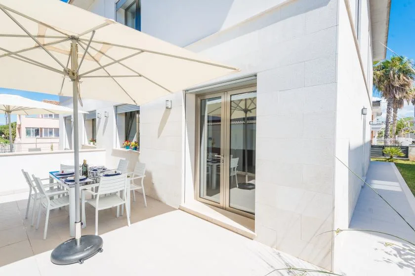 A sunlit outdoor dining area with a large patio umbrella beside a glass door.