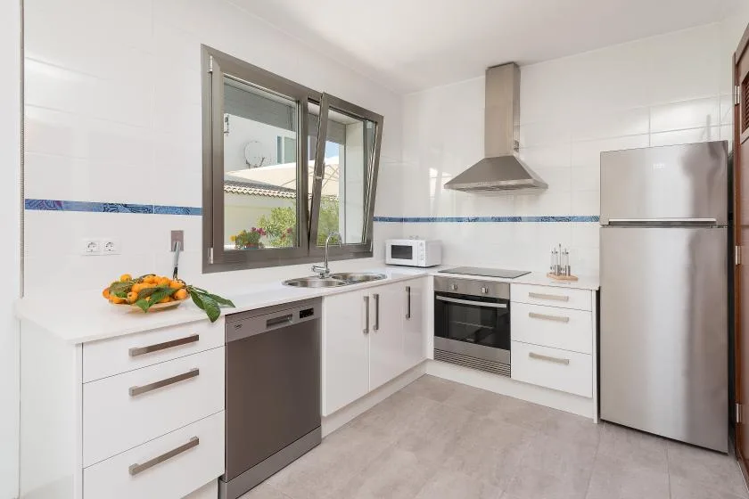 A bright kitchen with white cabinets, a stainless-steel refrigerator, and a window above the counter.