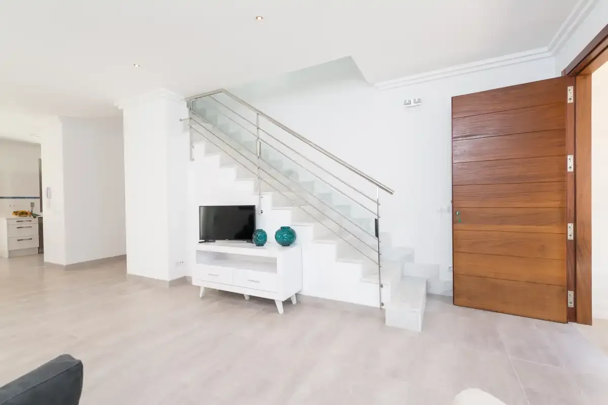A bright living area features a staircase with a glass railing and a television.