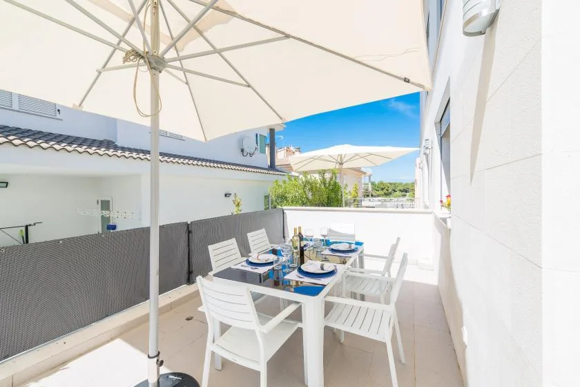 An outdoor dining area with white seating beneath a large umbrella.