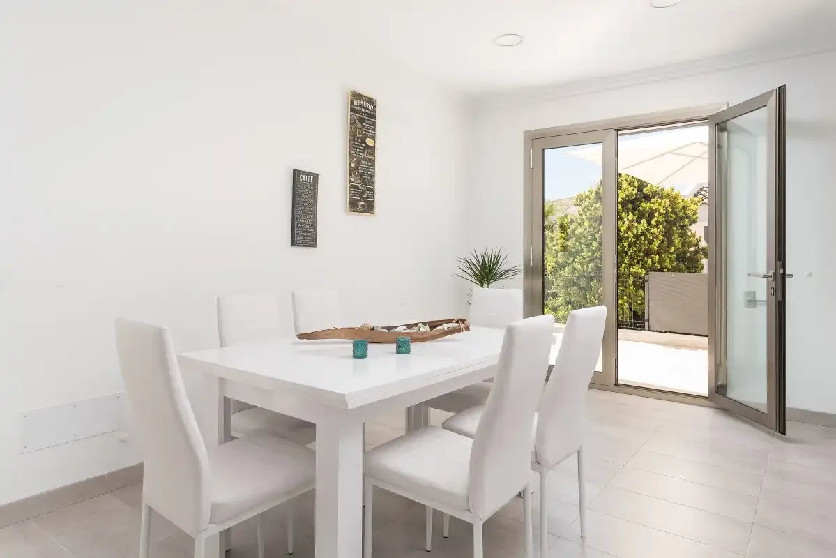A bright dining area with a white table and open glass doors.
