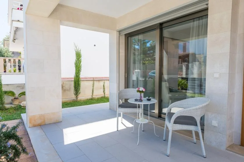 A covered patio with two seats and a small table beside glass doors.