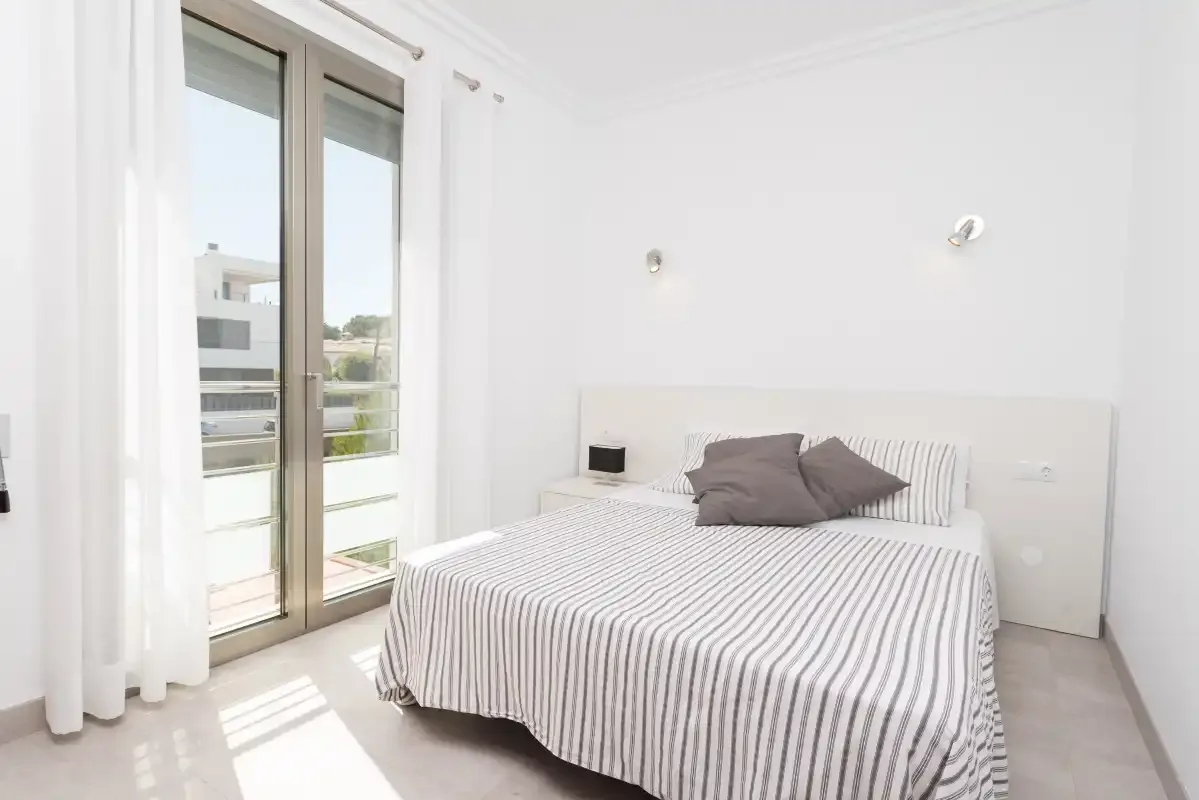 A bright bedroom with a striped bed beside tall glass doors.