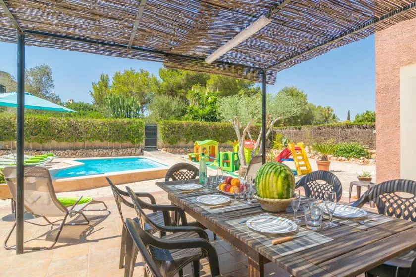 A shaded outdoor dining area overlooks a swimming pool and garden.