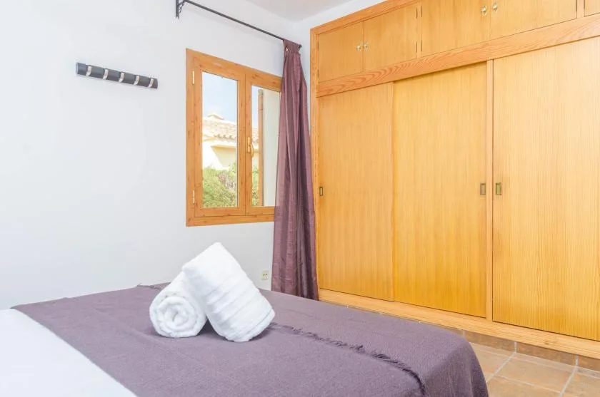 A bedroom with a bed, folded towels, a window, and wooden storage cabinets.