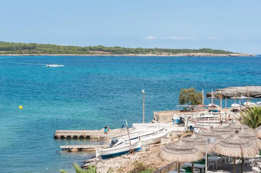A seaside beach with turquoise water, small boats, and thatched umbrellas.