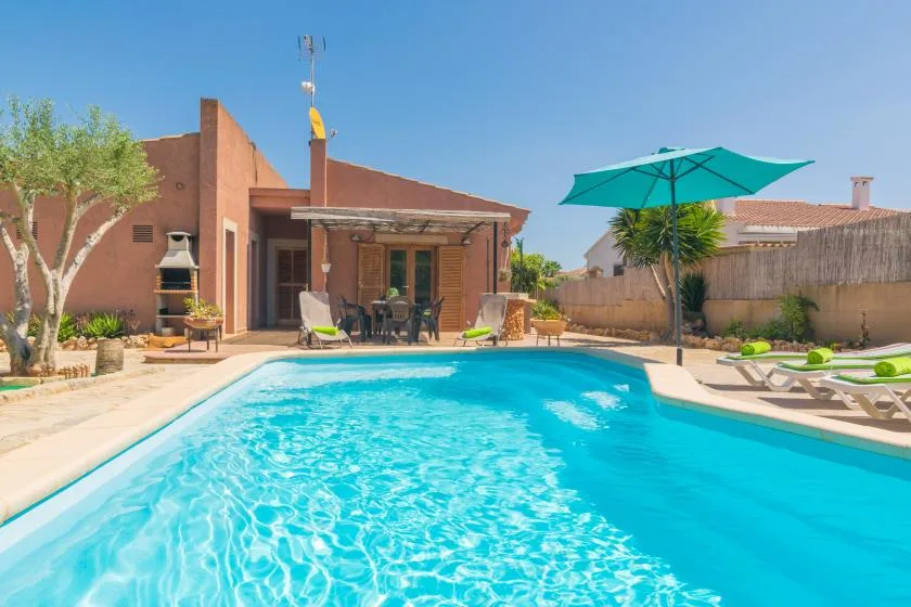 Una piscina junto a un patio con asientos y una sombrilla grande.