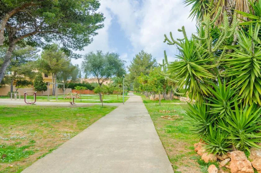 A paved walkway runs through a landscaped garden with trees and shrubs.