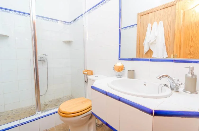 A tiled bathroom with a shower, toilet, and sink beneath a mirror.