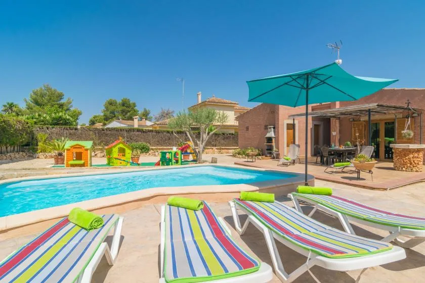 An outdoor pool with striped loungers and a large turquoise umbrella beside a patio.