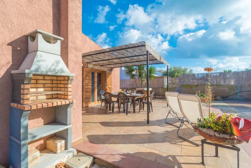 A tiled outdoor patio with a brick barbecue, dining table, and lounge chairs.