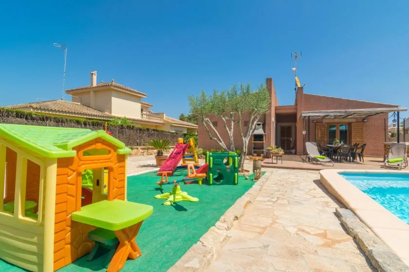 A sunny outdoor scene with a children's play area beside a swimming pool and patio.