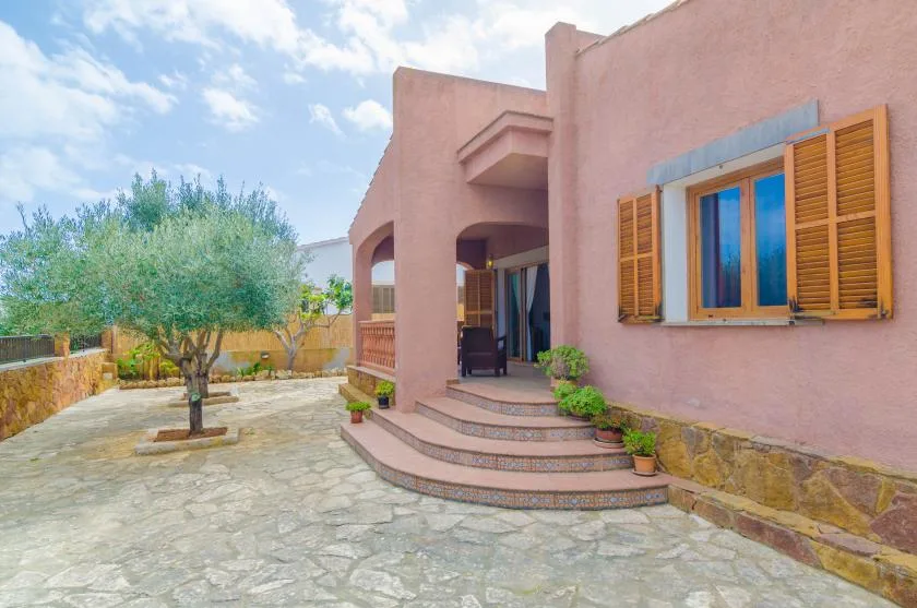 A pink stucco house opens onto a stone-paved courtyard with a tree.