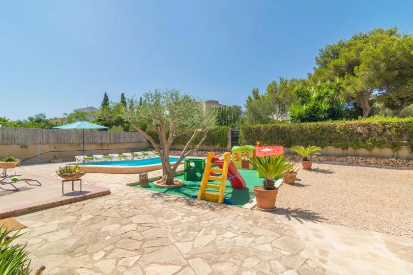 An outdoor pool area with a colorful play structure and paved seating space.