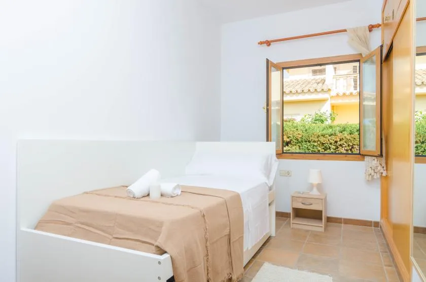 A bedroom with a bed beside an open window overlooking greenery.