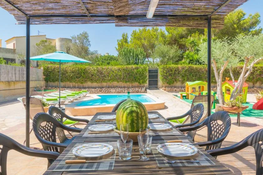 A shaded outdoor dining area overlooks a swimming pool and garden.